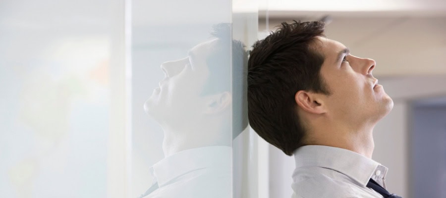 Businessman leaning against wall, head tilted back, appearing stressed or contemplative.