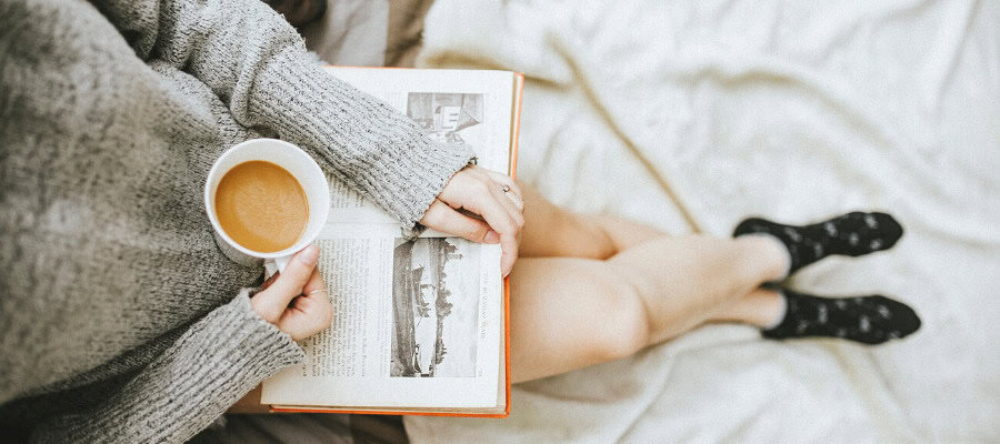 Woman relaxing at home, reading a book and enjoying a warm beverage.