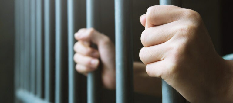 Close-up of hands gripping prison bars.