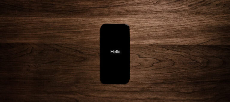 Black smartphone displaying "Hello" on a dark wood surface.