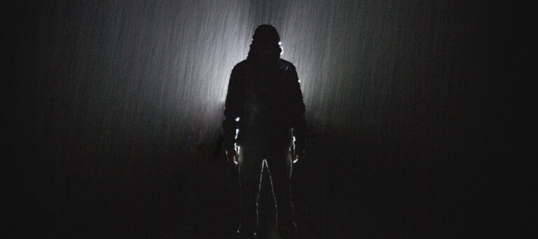 Silhouette of a person in a hooded jacket standing in heavy rain.