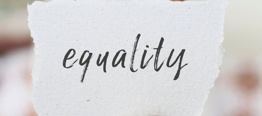 Hand holding a piece of paper with the word "equality" written on it.