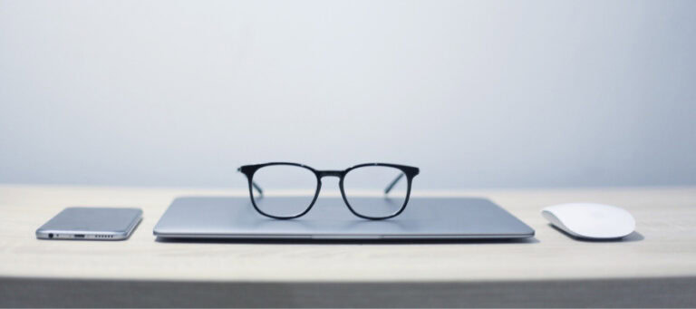 Laptop, eyeglasses, and wireless mouse on a desk.