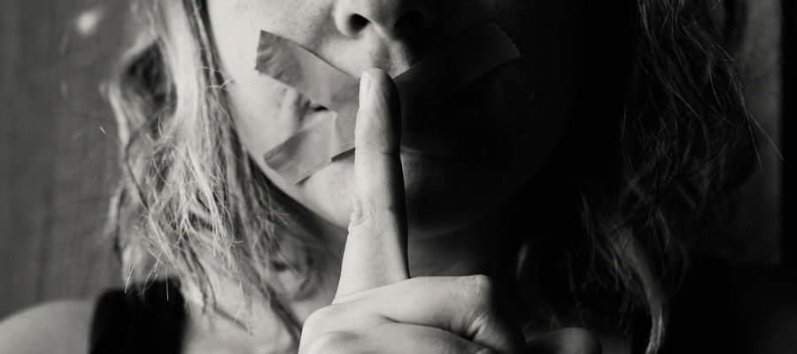 Close-up of a woman's mouth covered with tape, finger to lips.