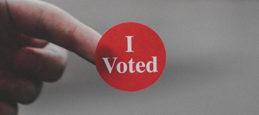 Finger pointing to "I Voted" sticker.