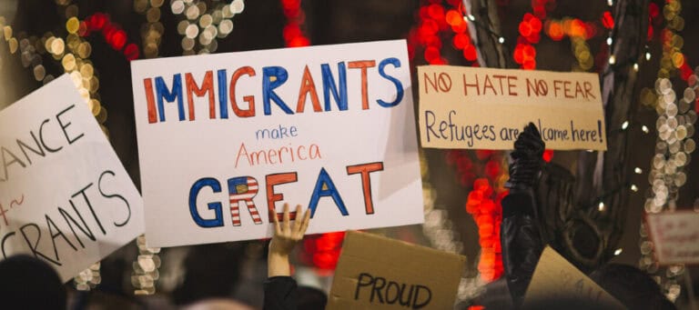 Protestors hold signs reading "Immigrants make America Great," "No Hate No Fear," and "Refugees are welcome here.