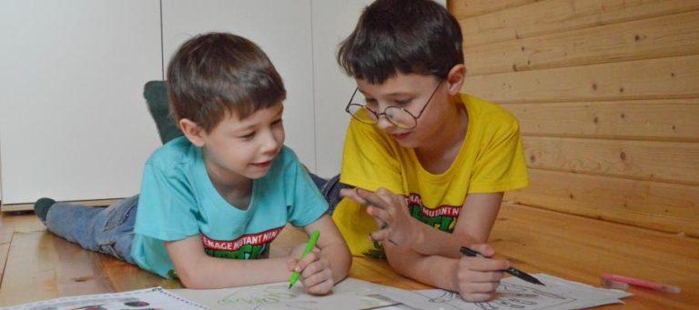 Two boys collaborate on a drawing, showcasing childhood creativity.