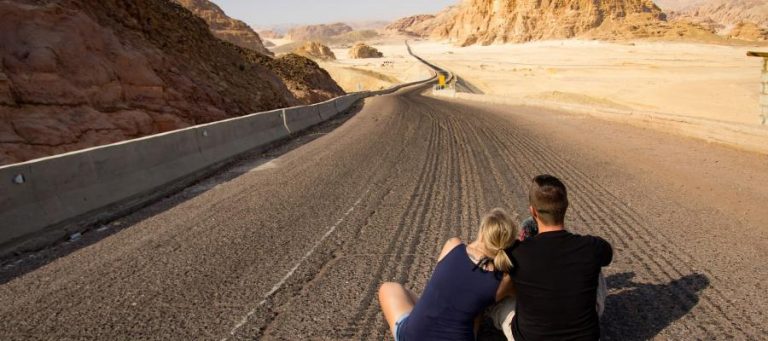 Couple sitting on a desert road, gazing at the landscape.