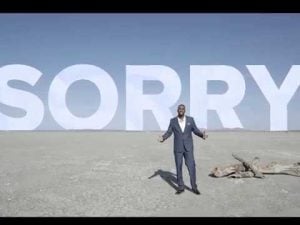 Man standing in a desolate landscape under a sky with the word "SORRY" written in large letters. What do we owe future generations?