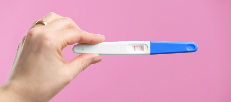 Hand holding a positive pregnancy test. Two lines are visible.