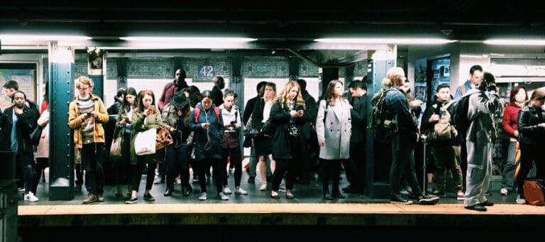 Crowded subway platform with diverse commuters using smartphones.