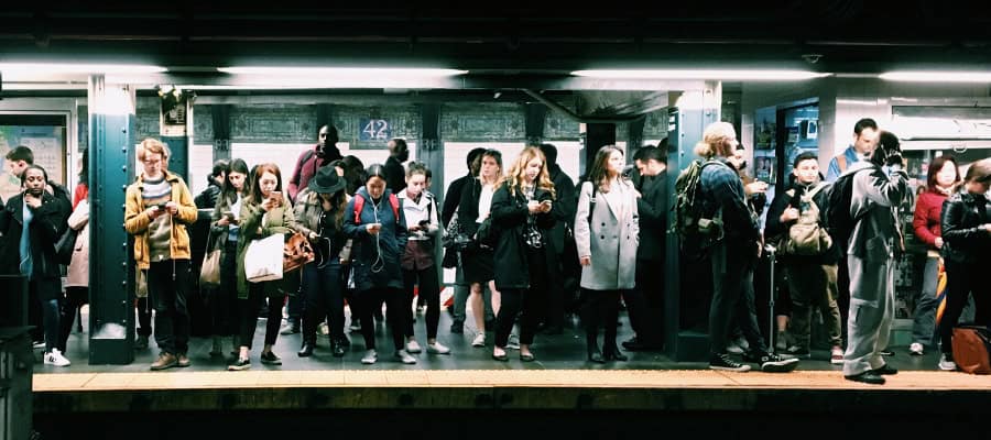 Crowded subway platform with diverse commuters using smartphones.