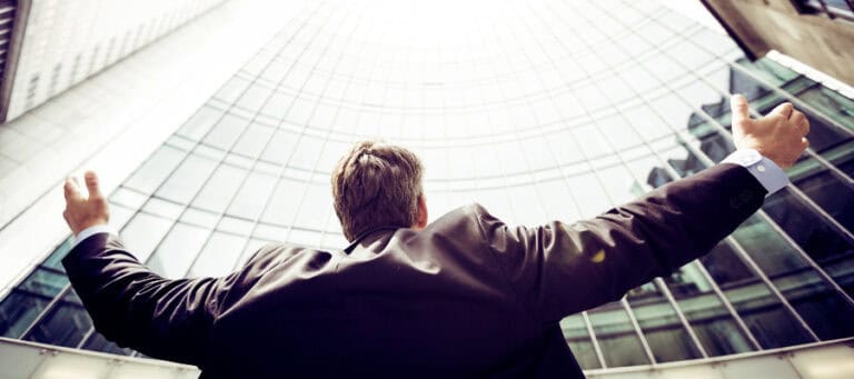 Businessman with arms outstretched, looking up at a modern skyscraper.