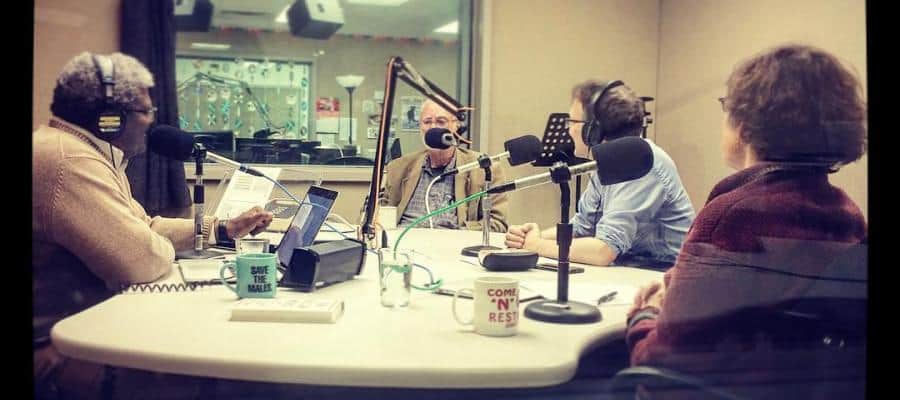 Four people participate in a radio show recording, seated around a table with microphones.