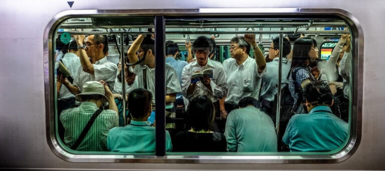 Crowded Japanese commuter train, passengers reading and standing.
