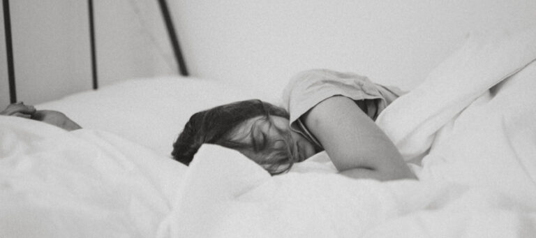 Woman sleeping peacefully in bed, covered by white sheets.