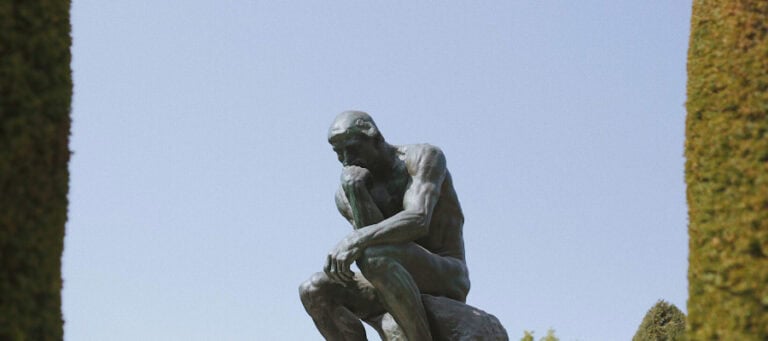 Bronze sculpture of a seated man contemplating, Rodin's "The Thinker.