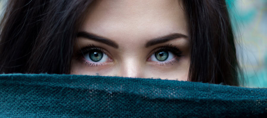 Close-up of a woman's expressive green eyes partially hidden behind a teal fabric.