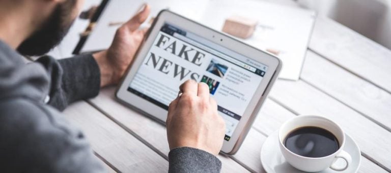 Person reading "Fake News" on a tablet, coffee nearby.