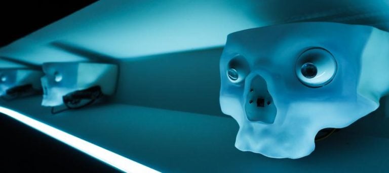 Row of stylized skull sculptures with glowing eyes, illuminated in blue light.