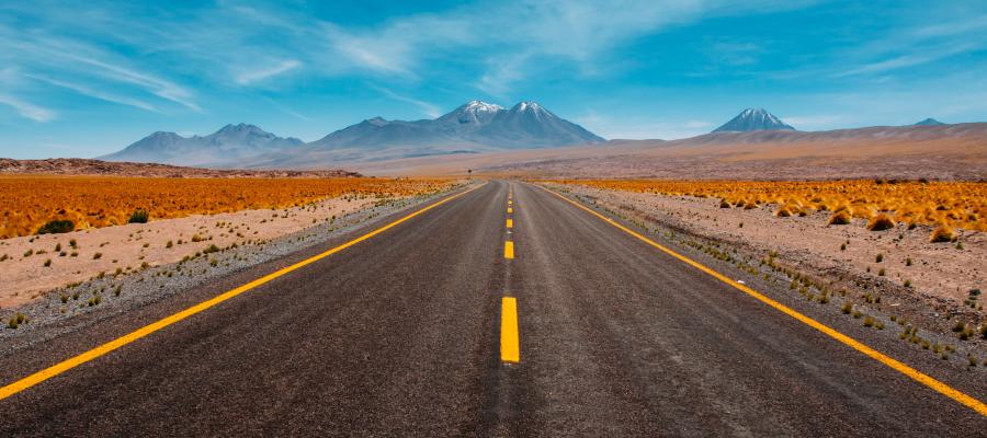 Open road stretching towards distant mountains under a blue sky.