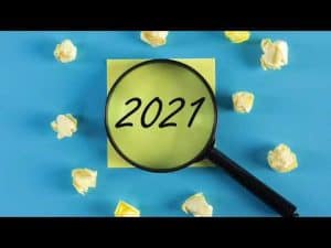 Magnifying glass over 2021 on a yellow sticky note.