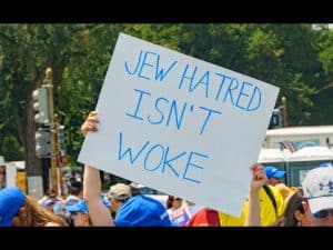 Protestor holds sign reading "Jew hatred isn't woke," illustrating the changing face of antisemitism.