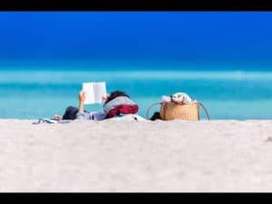 Person relaxing on a beach, reading a book from their 2023 summer reading list.