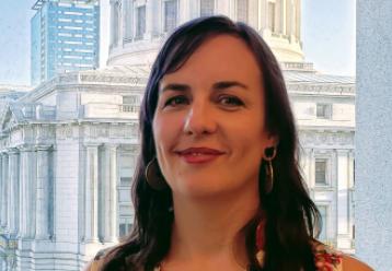 Headshot of a woman, smiling, in front of a city hall building.