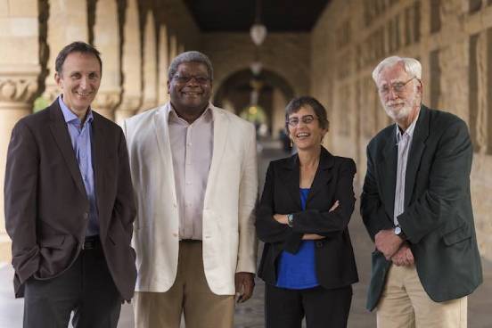 Four smiling academics, two men and two women, stand in an academic hallway. About us.