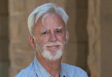 Headshot of a smiling older man with gray hair and beard.