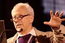 Older man with glasses giving a presentation, discussing science and religion.