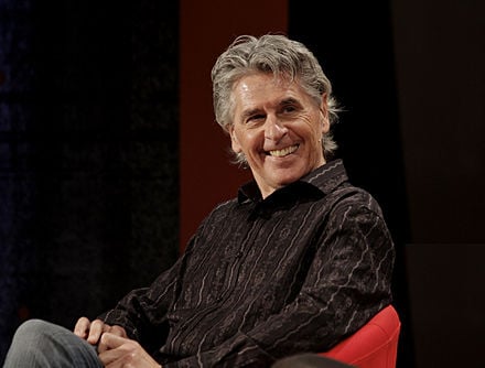 Smiling man with graying hair, seated and looking towards the viewer.