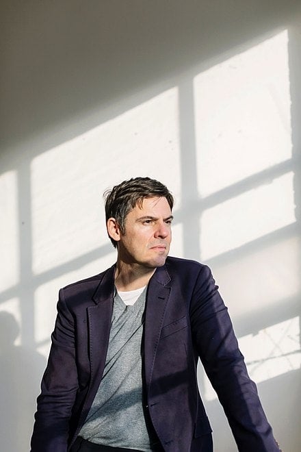 Man in blazer thoughtfully looking away, sunlight illuminating the background.
