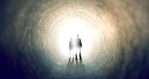Silhouetted couple walking toward a bright light at the end of a tunnel, symbolizing the afterlife and immortality.