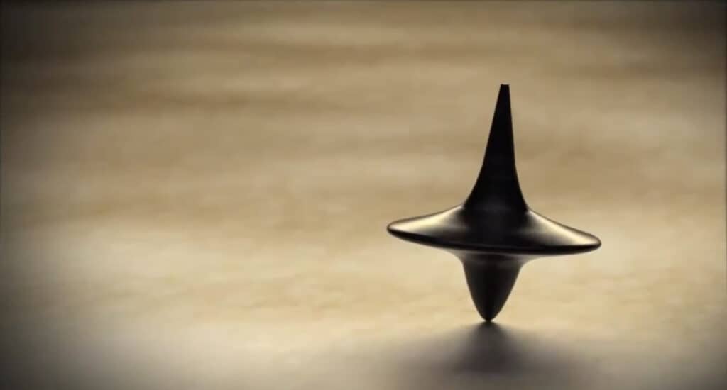 Black spinning top on beige surface; a symbol of skepticism and uncertainty.