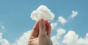 Hand holding a cotton ball resembling a cloud against a blue sky. Illustrates imagination.