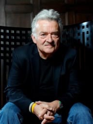 Portrait of older man with gray hair, wearing a black jacket and jeans.