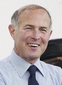 Portrait of a smiling man in a light blue striped shirt and dark tie.