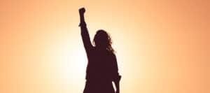 Silhouette of a woman raising her fist in the air at sunset, symbolizing female empowerment and feminism.