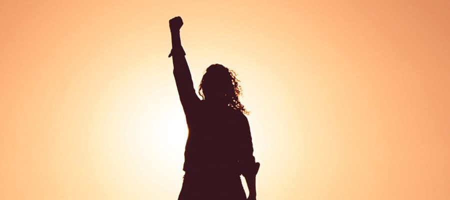 Silhouette of a woman raising her fist in the air at sunset, symbolizing female empowerment and feminism.