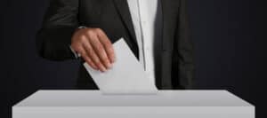 Person in suit dropping ballot into a ballot box. Is this democracy?