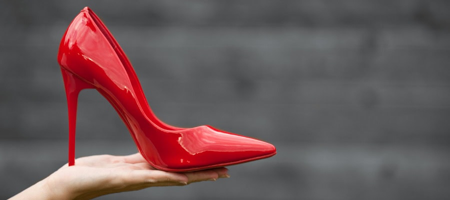 Woman's hand holding a single red high-heeled shoe.