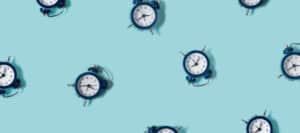 Multiple blue alarm clocks scattered on a light blue background. Time management concept.