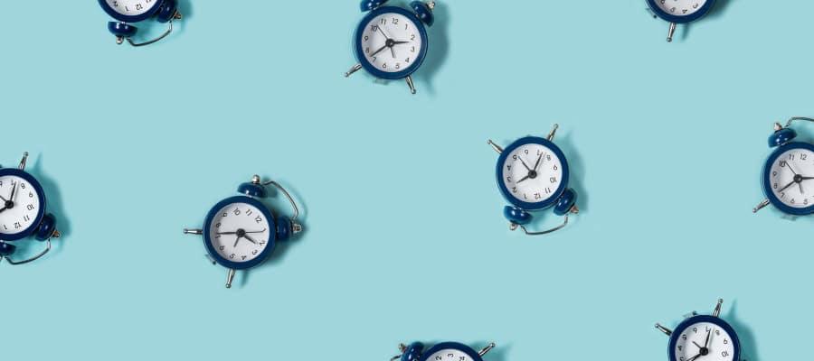 Multiple blue alarm clocks scattered on a light blue background. Time management concept.