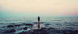 Silhouette of a person standing on a pier overlooking the ocean at sunset.