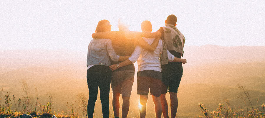 Four friends embrace at sunset, showcasing the strength of their friendship.