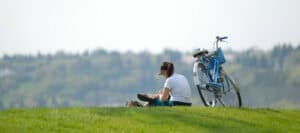 Woman relaxing outdoors with a blue bicycle, enjoying a summer day.