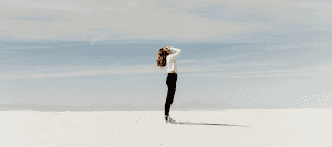 Woman standing in white sand, hands on head, showcasing human contemplation.