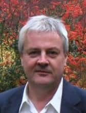 Headshot of a middle-aged man with short gray hair, wearing a dark blazer.